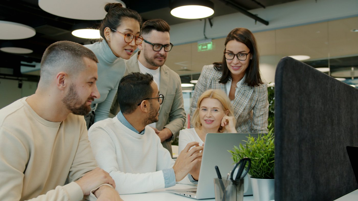 A diverse team of colleagues smiling and working together around a laptop